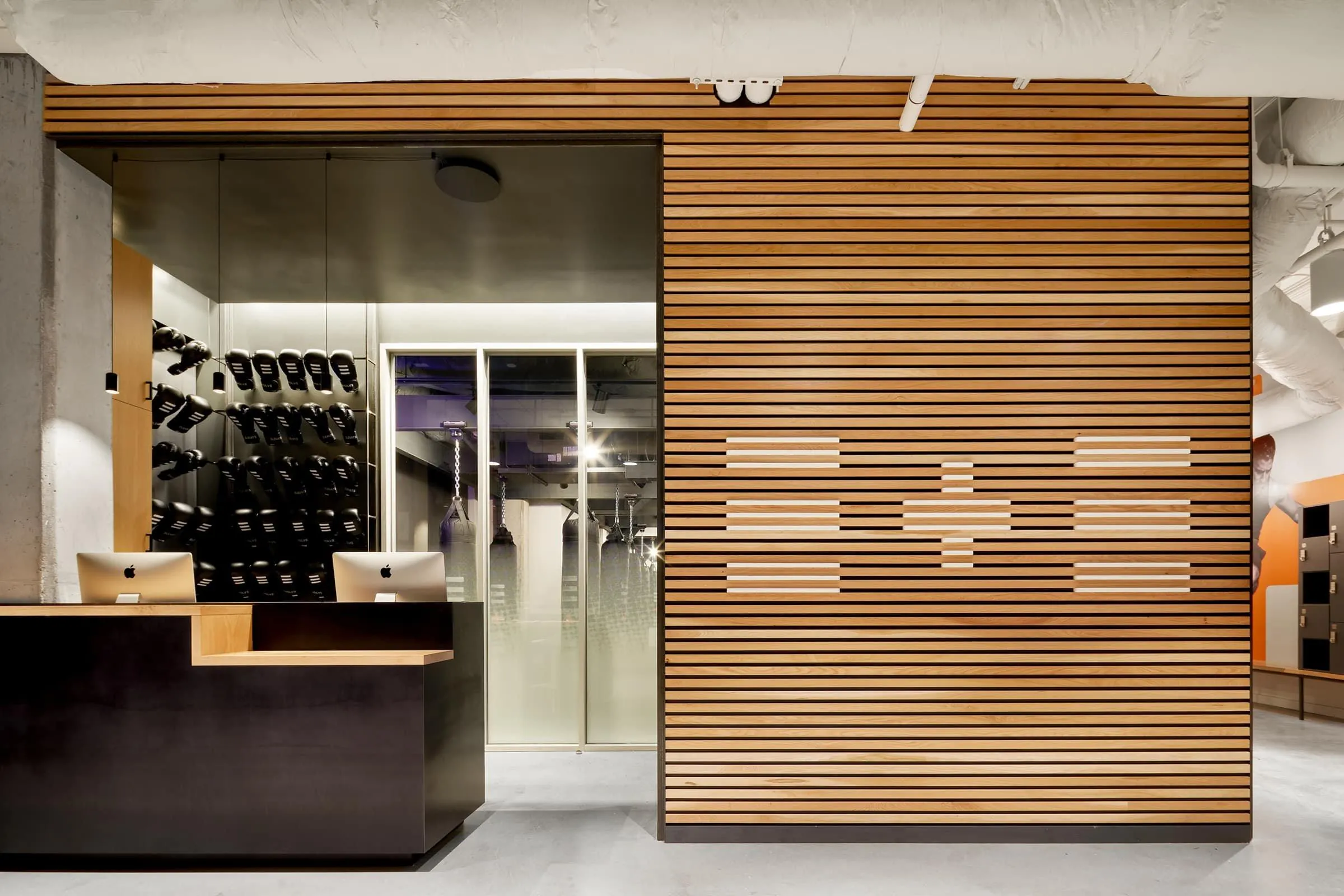Modern gym reception with vertical wood-look wall panels, dark front desk, and boxing training area